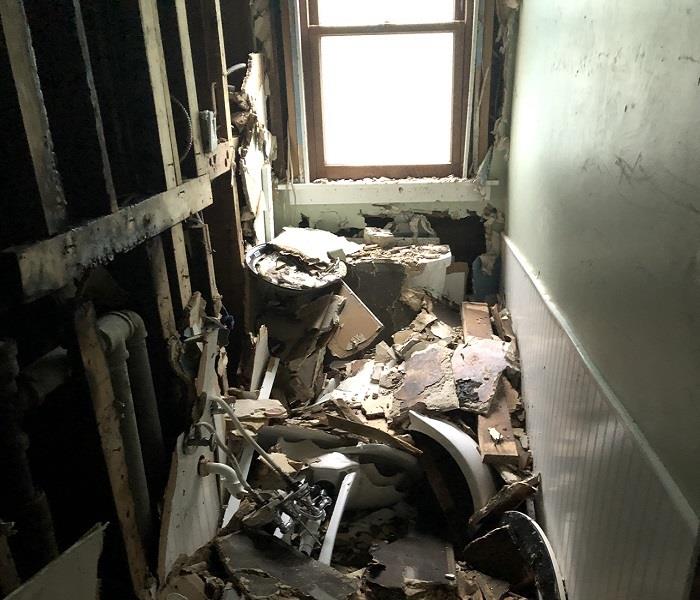Small half bathroom with exposed pipes and burned walls. Parts of a sick and debris covering entire floor.