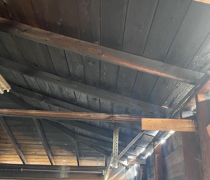 The inside of a roof that is burned black with holes on the wall letting sunlight in