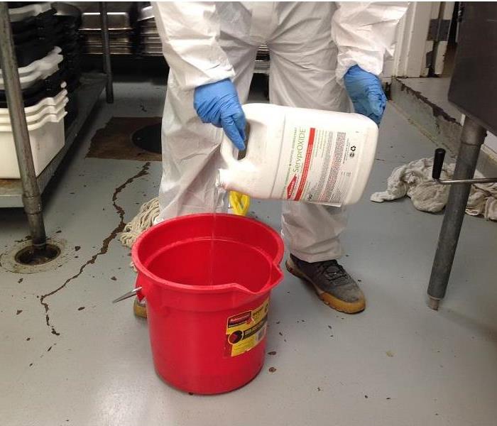 Crew member in hazmat suit pouring disinfectant into a bucket 