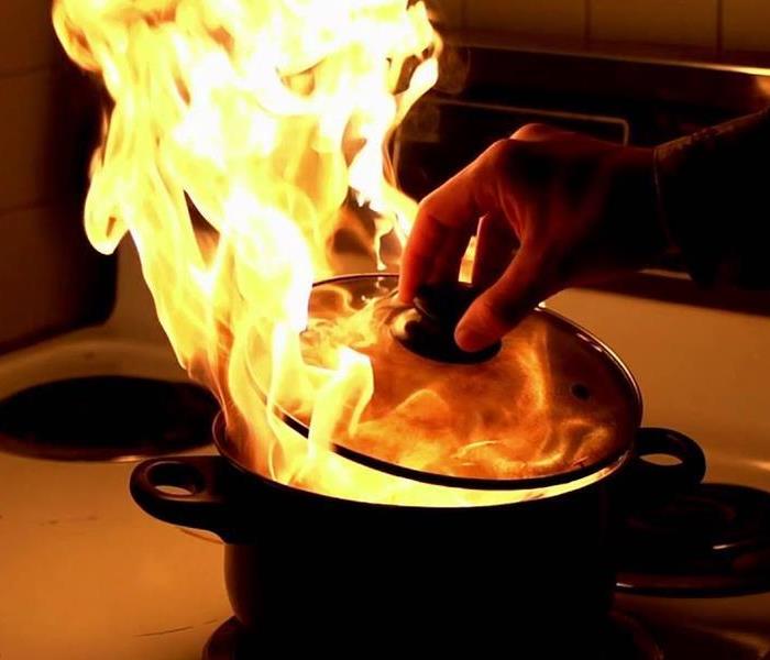 Flames in a pan and someone is putting a lid over it. 